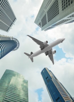 Tall city buildings and a plane flying overhead in morning